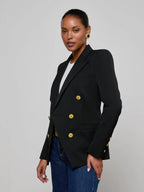 Woman wearing a black blazer with gold buttons on a gray background