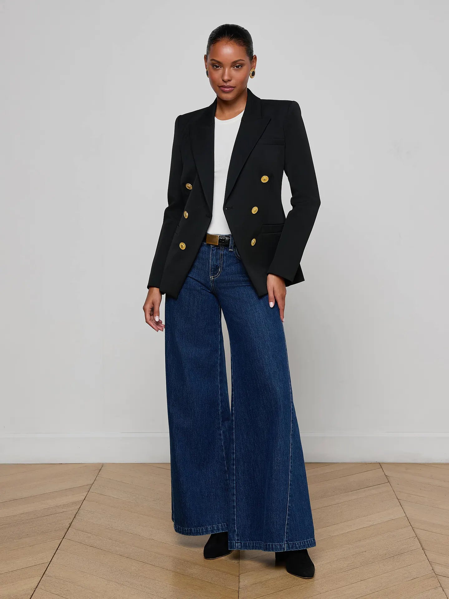 Woman wearing a black blazer with gold buttons and blue jeans on a plain background