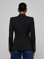 Person wearing a black blazer with gold buttons on a gray background