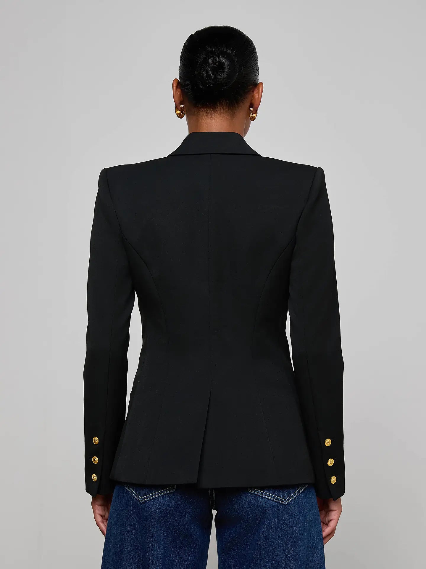 Person wearing a black blazer with gold buttons on a gray background