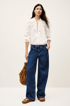 Woman wearing a white blouse and blue jeans, holding a brown bag on a white background