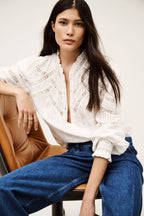 Woman wearing a white blouse and blue jeans sitting on a chair.