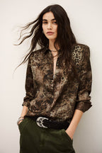 Woman wearing a patterned shirt with a belt and pants against a plain background