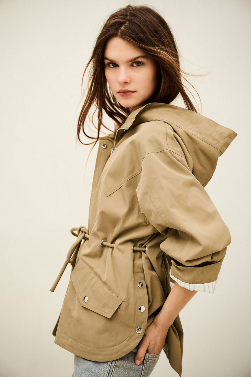 Woman wearing a beige jacket with a hood on a plain background