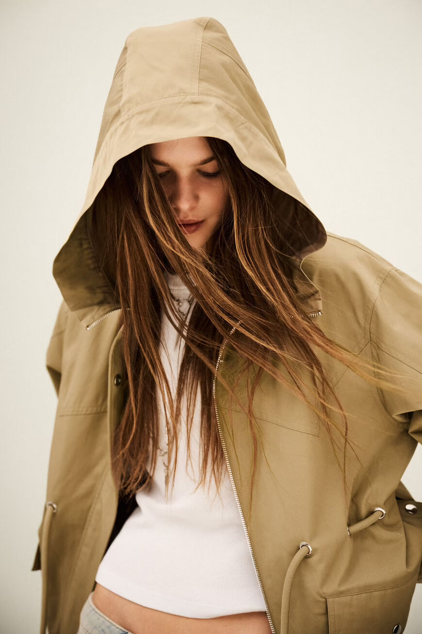 Woman wearing a beige hooded jacket with a plain background