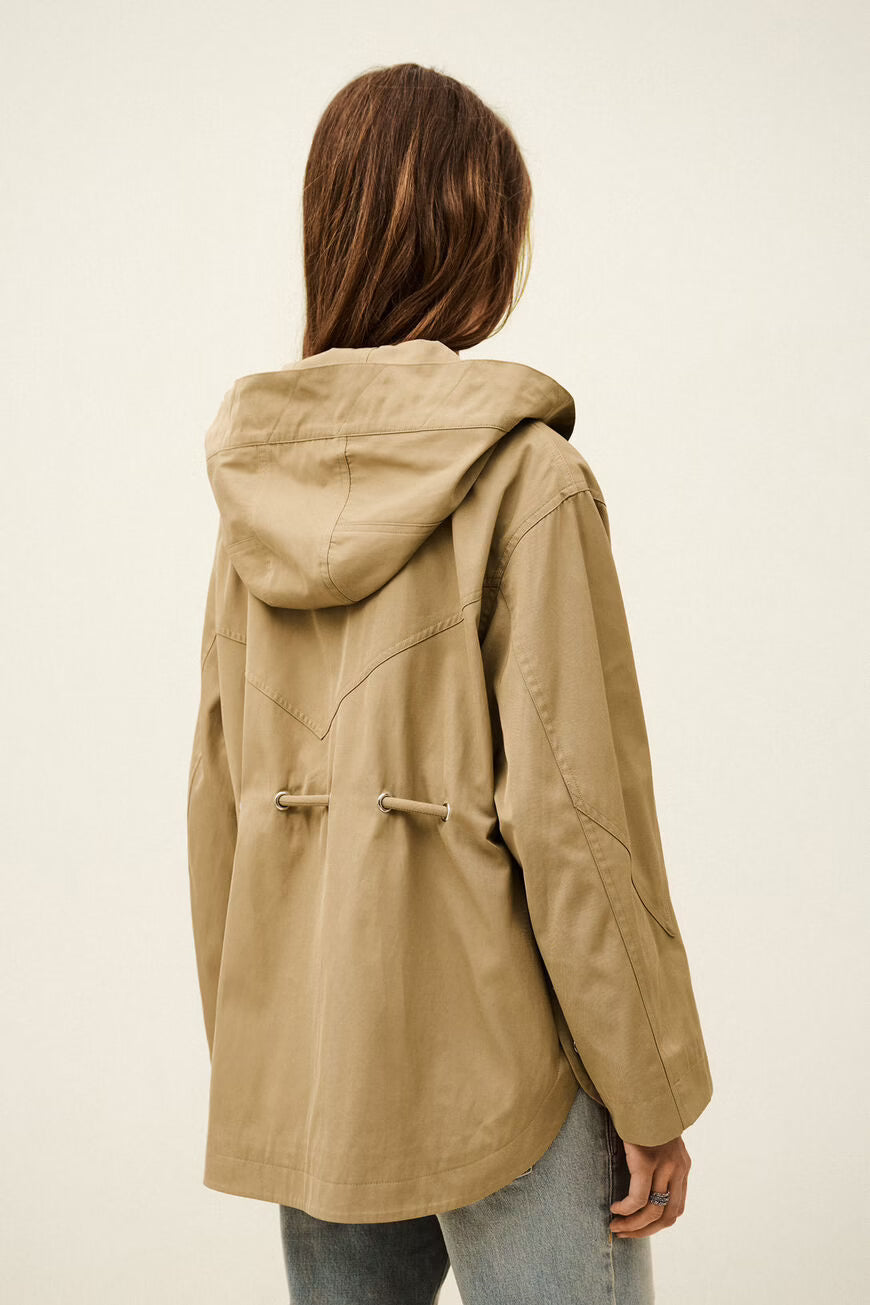 Person wearing a beige hooded jacket on a plain background
