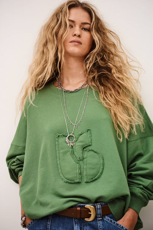 Woman wearing a green oversized sweatshirt with a pocket design on a plain background