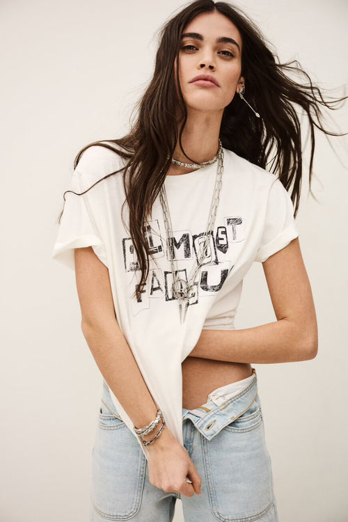 Woman wearing a white t-shirt with text and light blue jeans against a plain background