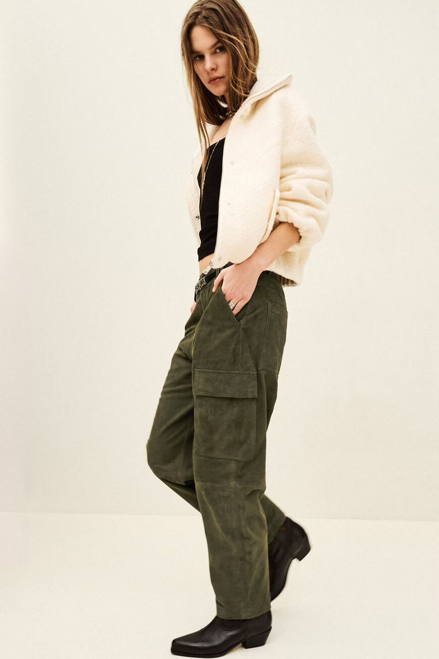 Person wearing a beige cardigan, black top, green cargo pants, and black boots on a white background
