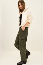 Person wearing a beige cardigan, black top, green cargo pants, and black boots on a white background