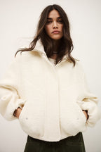 Woman wearing a white oversized jacket against a plain background