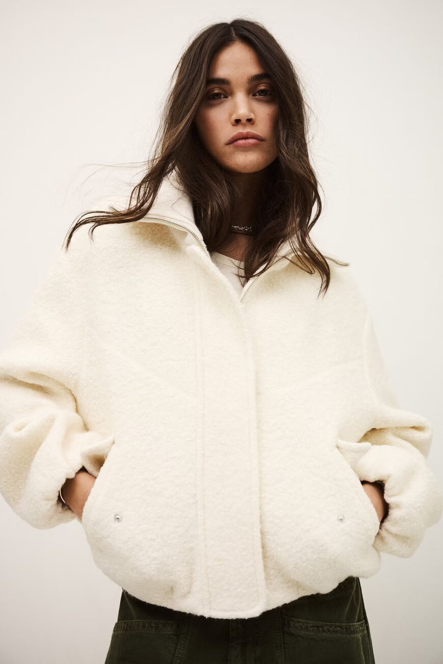 Woman wearing a white oversized jacket against a plain background