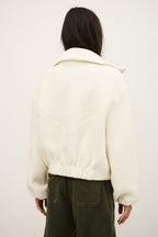 Person wearing a white textured jacket and green pants against a plain background