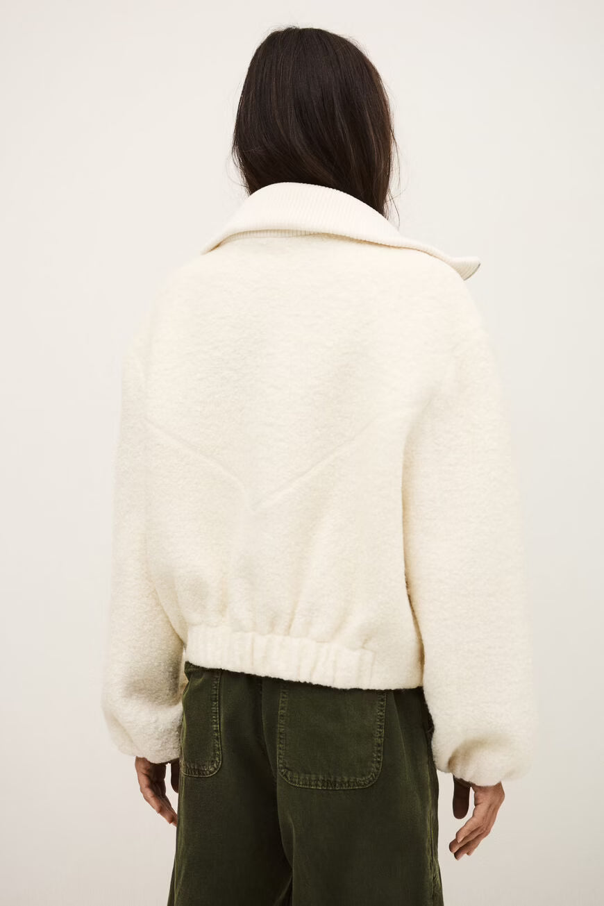 Person wearing a white textured jacket and green pants against a plain background