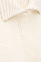 Close-up of a cream-colored garment with a zipper detail on a light beige background