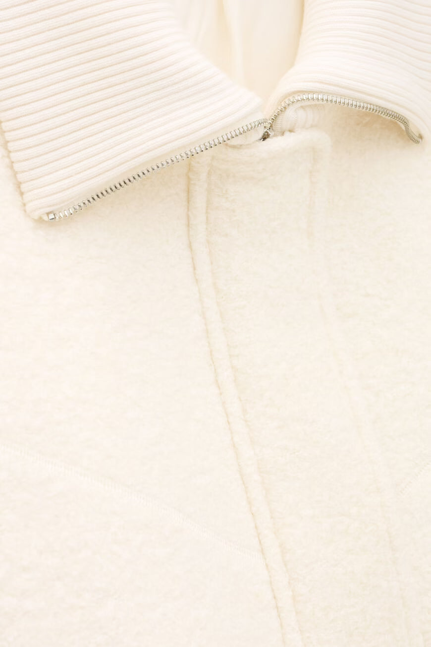 Close-up of a cream-colored garment with a zipper detail on a light beige background