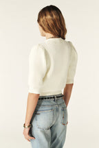 Person wearing a white textured sweater and light blue jeans on a plain background