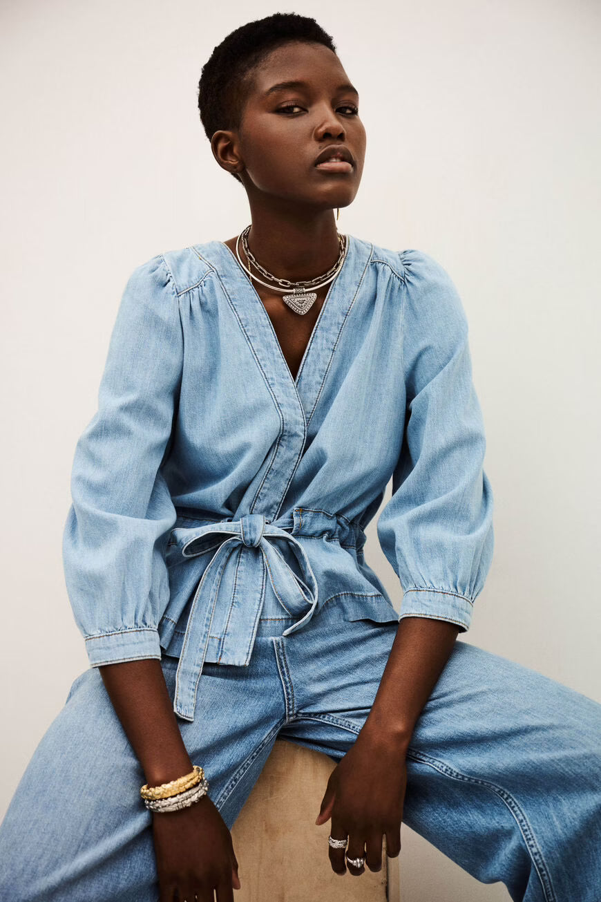Woman wearing a blue denim outfit sitting against a plain background