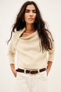 A woman modeling a cream-colored knit sweater with a half-zip neckline, paired with white jeans and a brown belt, against a plain off-white background.