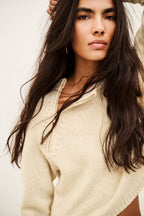 A close-up of a woman with long dark brown hair wearing a cream-colored knit sweater with a half-zip neckline.