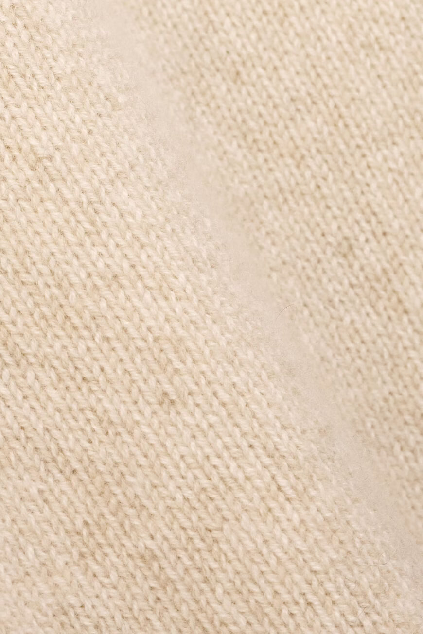 A close-up of a cream-colored knit fabric with a fine ribbed texture.