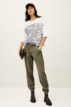 Woman wearing a white and black striped shirt, green pants, and a red cap on a white background