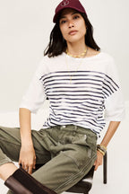 Woman wearing a striped shirt and cap sitting on a chair against a white background