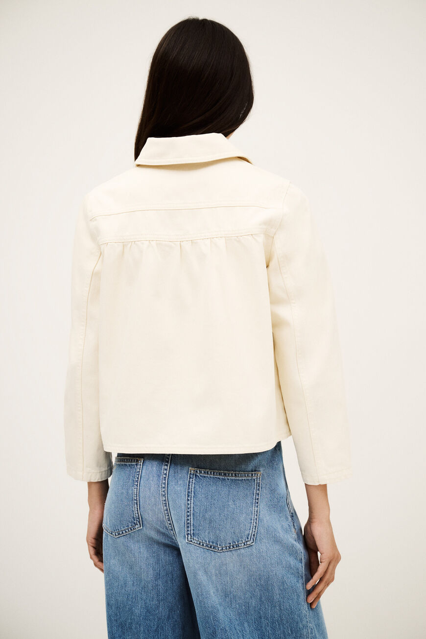 Person wearing a cream jacket and blue jeans on a white background