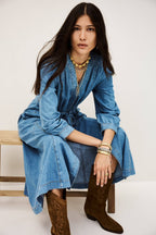 Woman wearing a blue denim dress and brown boots sitting on a white background