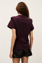 Person wearing a dark purple t-shirt and black leather shorts on a plain background