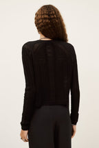 Person wearing a black ribbed sweater on a plain background