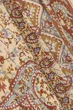 A close-up of a draped fabric with an intricate paisley pattern in muted tones of beige, brown, dusty blue, and purple.