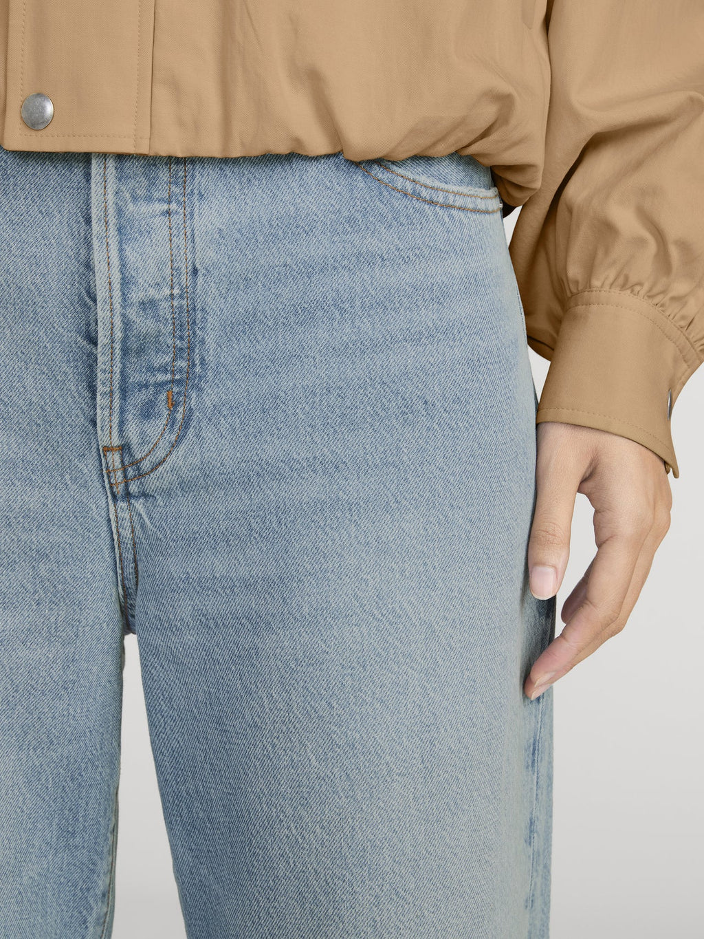Close-up of blue jeans and a tan jacket on a neutral background