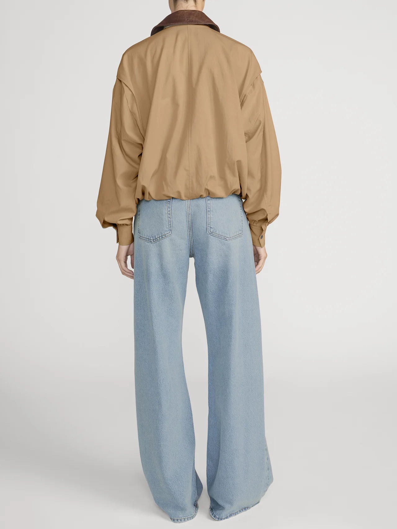 Person wearing a beige jacket and light blue jeans on a white background