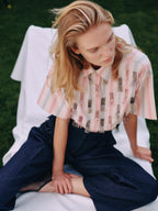 Woman sitting on a white chair wearing a patterned shirt and dark pants.