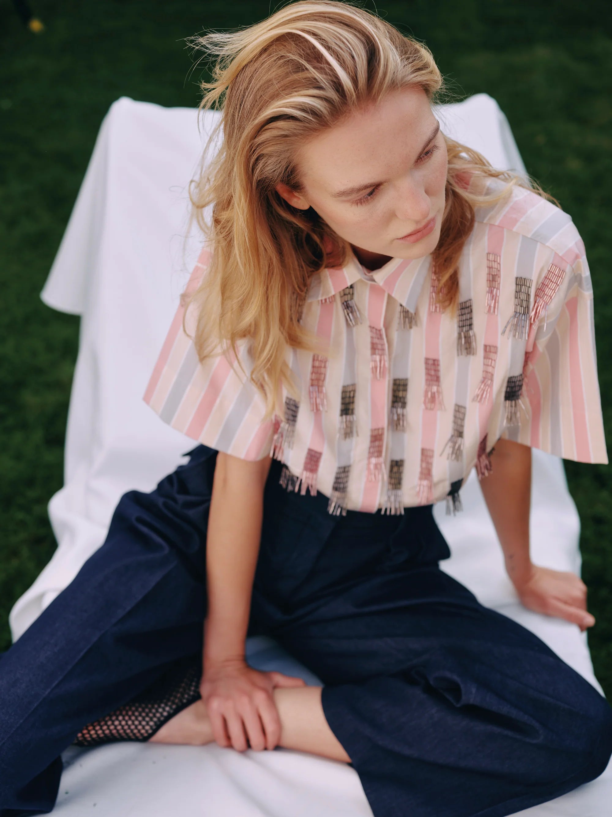 Woman sitting on a white chair wearing a patterned shirt and dark pants.