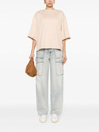 A model wearing a coral pink satin-detailed cotton T-shirt with short sleeves and a straight hem, paired with blue jeans.