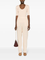 A model wearing high-waist straight leg trousers in a beige color, with an elasticated waistband, two side inset pockets, and two rear welt pockets. The trousers are presented against a white background.