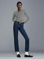 A person standing wearing mid-rise straight-leg ankle-length blue jeans with a striped black and white top, white socks, and black shoes.