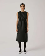 A model wearing a black sheath dress with a gathered waist, crew neck, and a V-neckline. The dress features a pleat on the back and an invisible side zip.