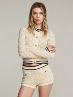 Woman wearing a cream lace outfit with gold buttons on a plain background