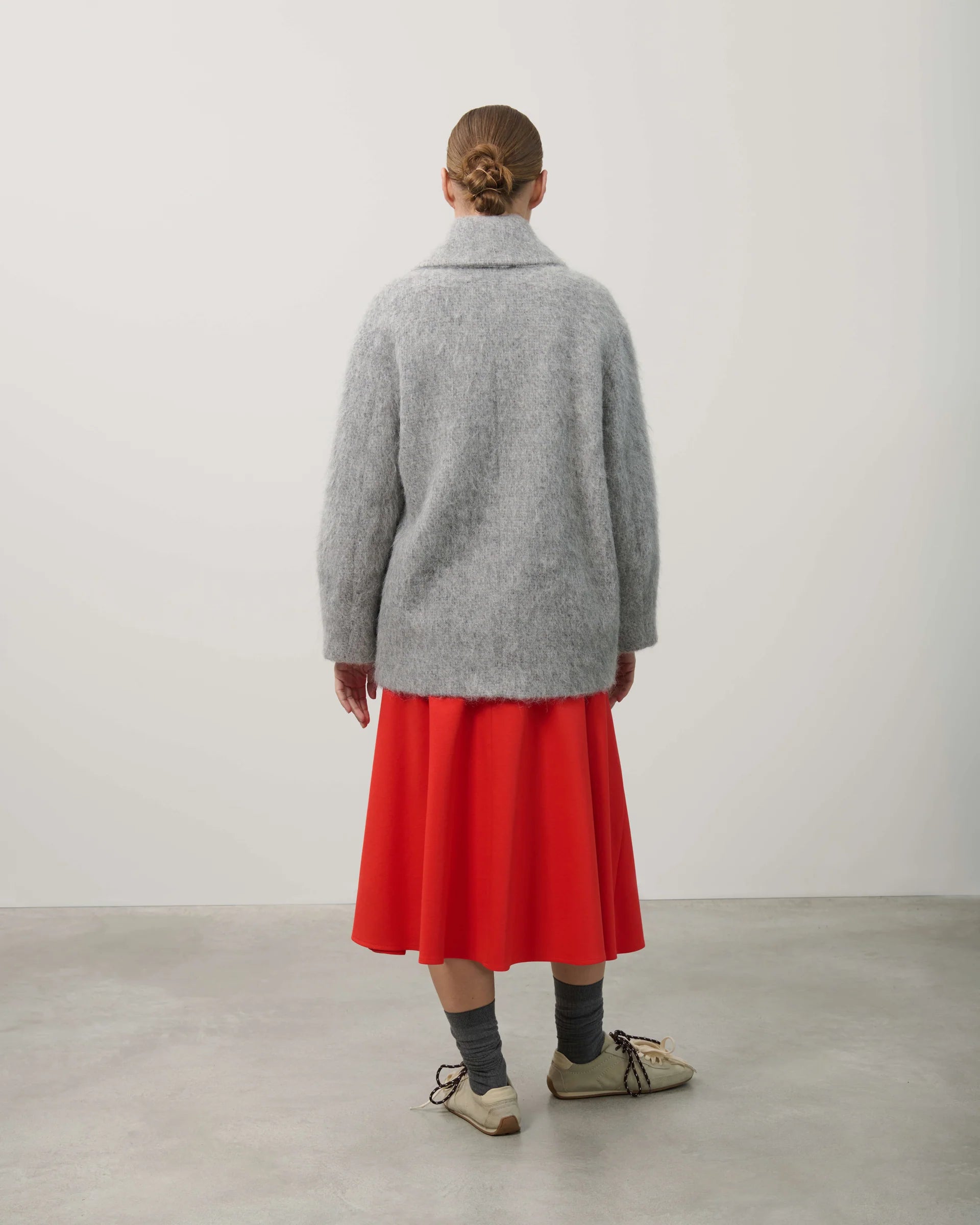 Person wearing a gray coat and red skirt standing against a plain background