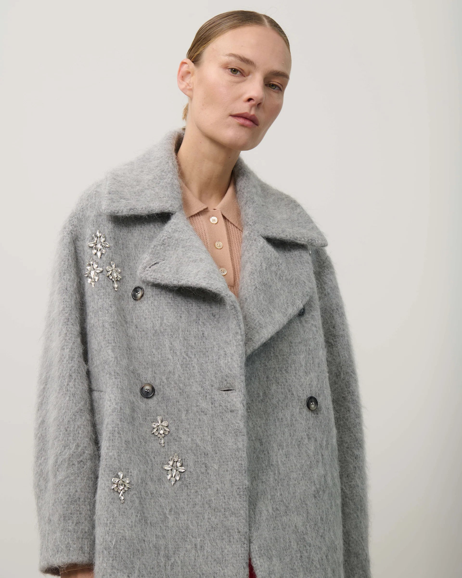 Woman wearing a gray coat with decorative elements on a plain background