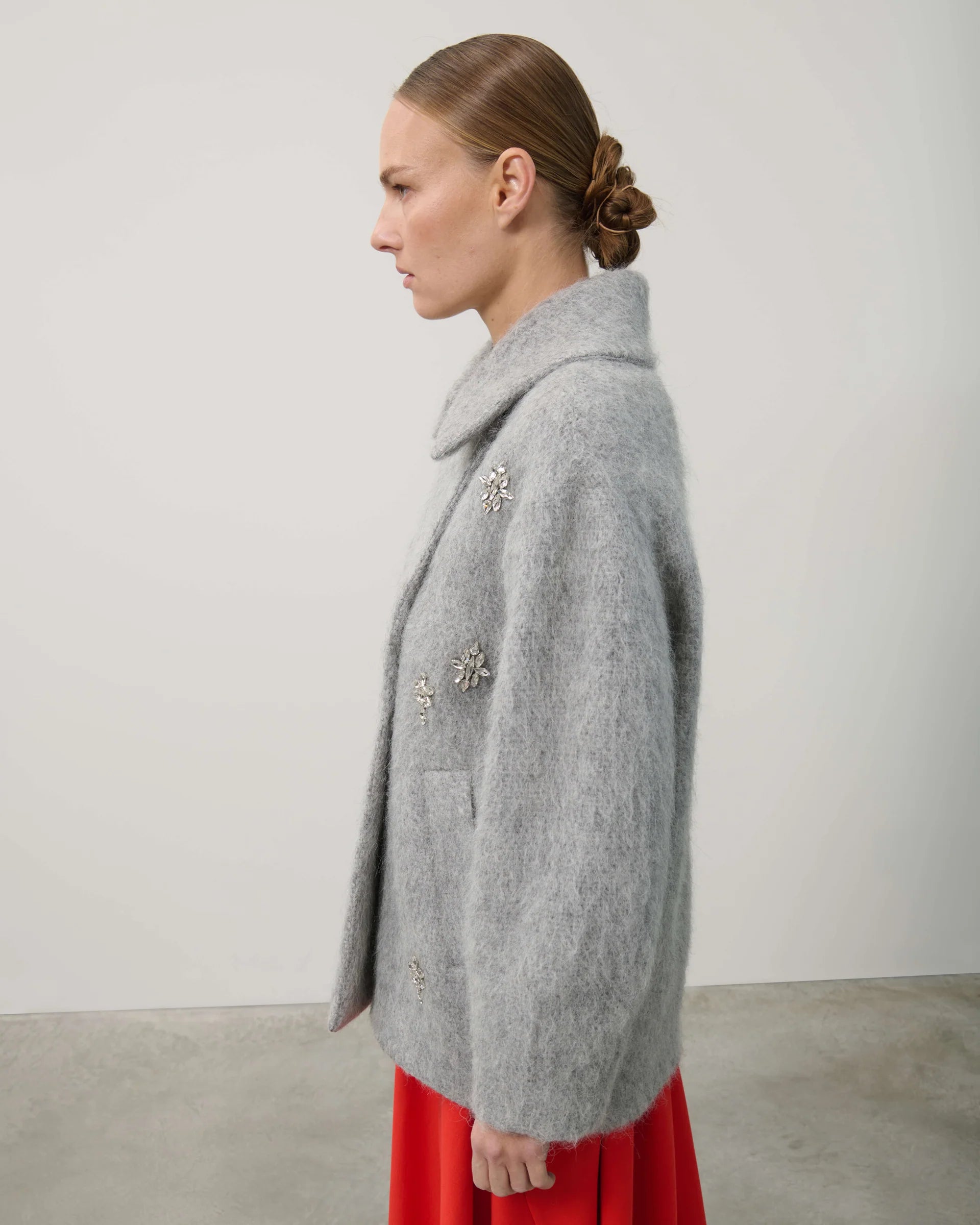 Woman wearing a gray coat with floral embellishments against a plain background
