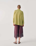 A model viewed from the back wearing a light olive green long-sleeve button-up shirt and dark purple wide-leg cropped pants with lace trim, paired with black sandals, against a light gray studio background.