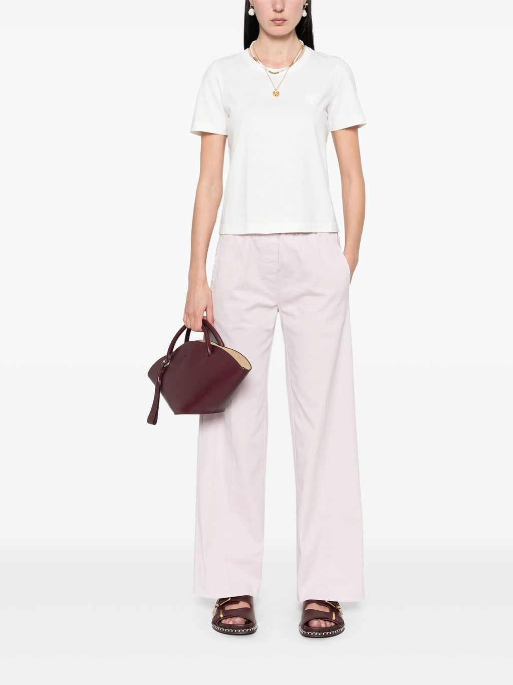Person wearing a white t-shirt and light pink pants holding a maroon handbag on a white background