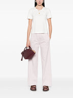 Person wearing a white t-shirt and light pink pants holding a maroon handbag on a white background