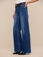 Person wearing blue wide-leg jeans with a beige background
