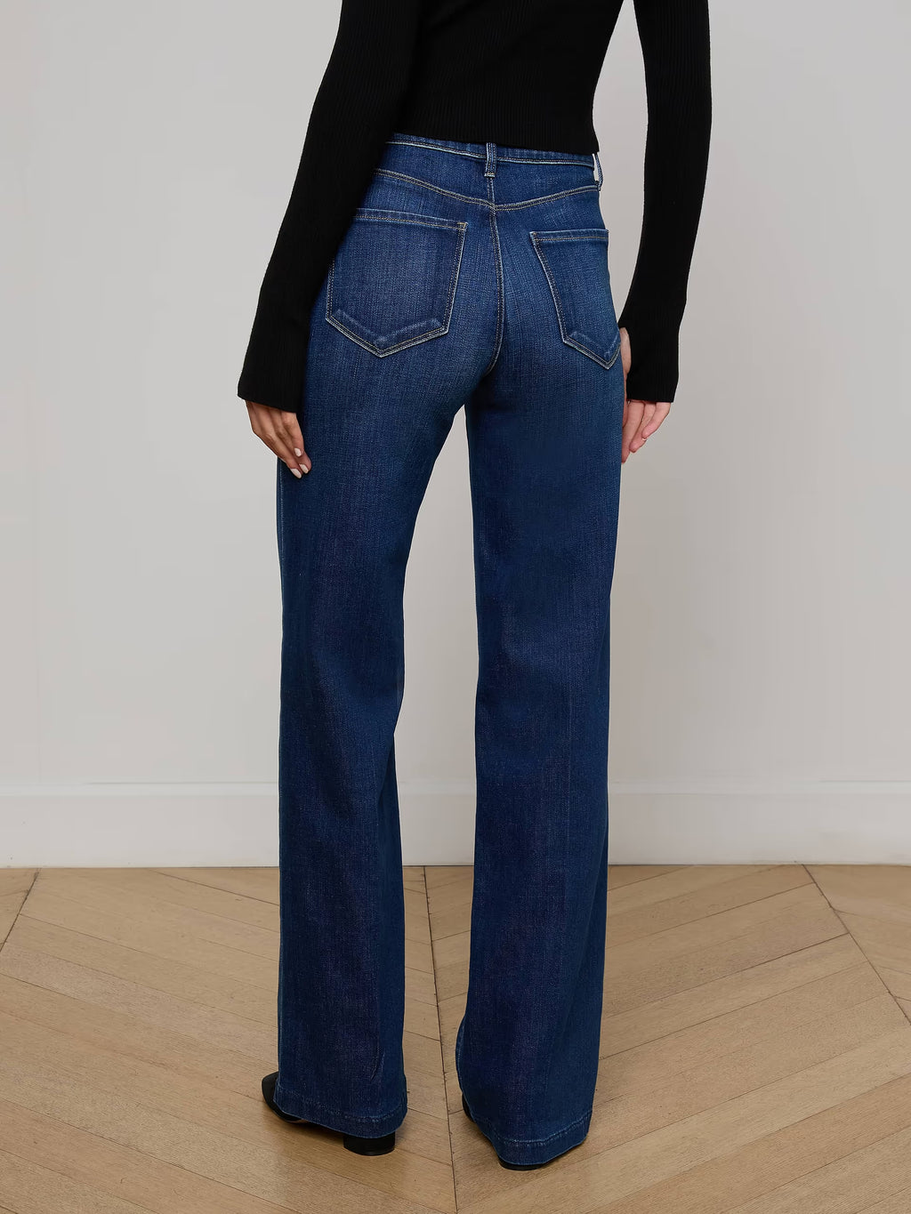 Person wearing blue jeans and a black top on a plain background