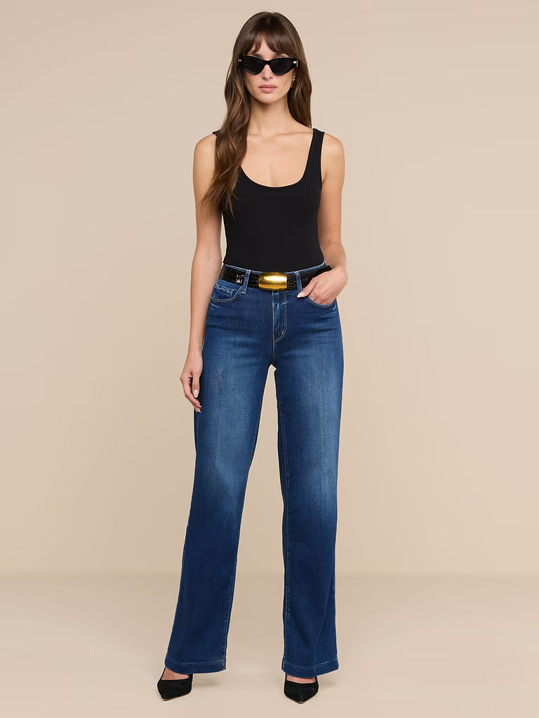 Woman wearing blue jeans and a black tank top on a beige background